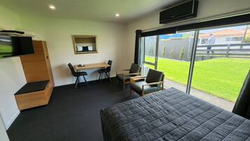 Una habitación de hotel con una cama, un escritorio con dos sillas, un televisor montado en la pared y un amplio ventanal con vistas al exterior.
