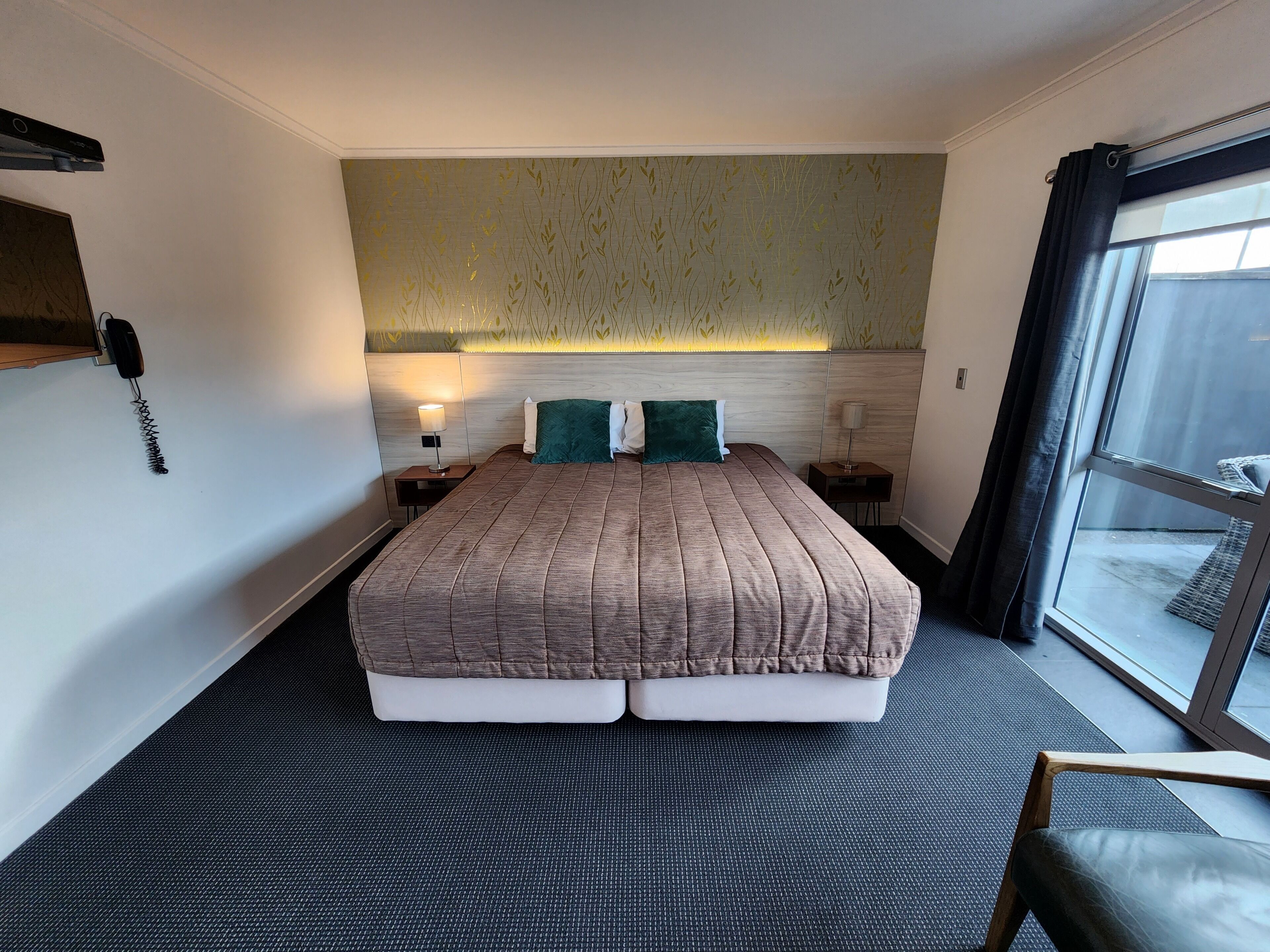 Quarto de hotel com uma cama grande, duas mesas de cabeceira com abajures, um telefone e vista para o exterior através de uma janela ampla.
