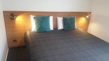 A hotel room with a wooden headboard, two pillows, and a dark patterned bedspread.