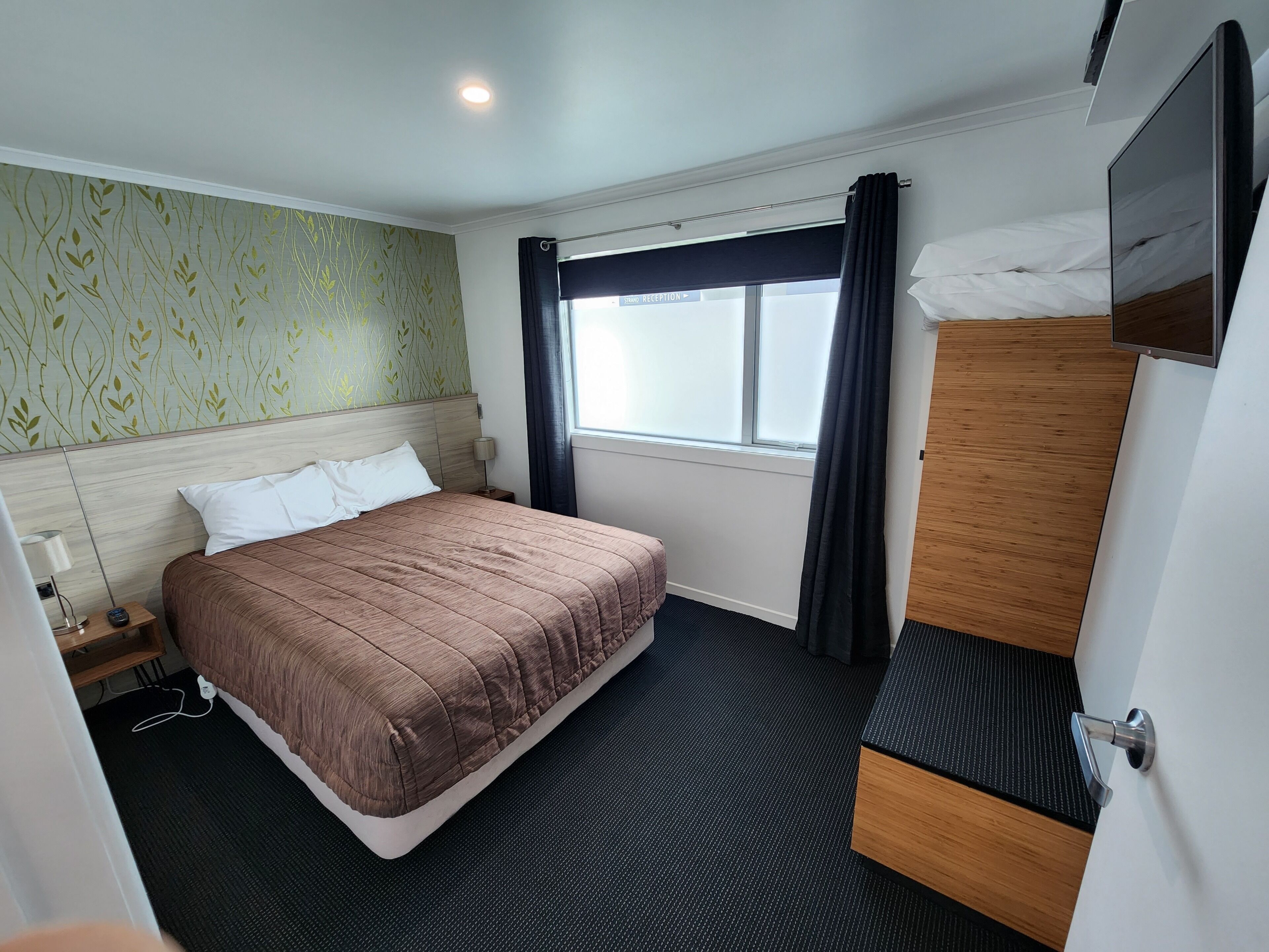 Una habitación de hotel con una cama, un armario de madera, un escritorio y una ventana con cortinas.