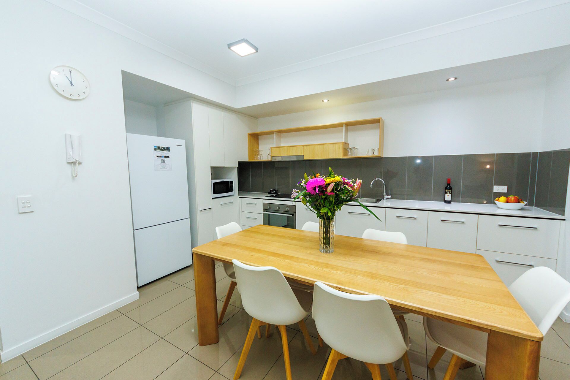 A modern kitchen with white cabinets, a wooden dining table, and a vase of flowers.