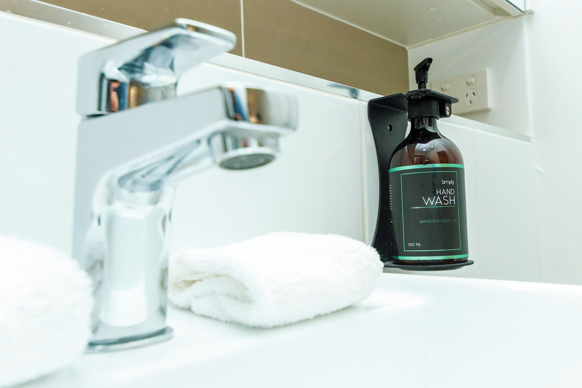A bathroom with a modern faucet, a bottle of hand wash soap, and a white towel.