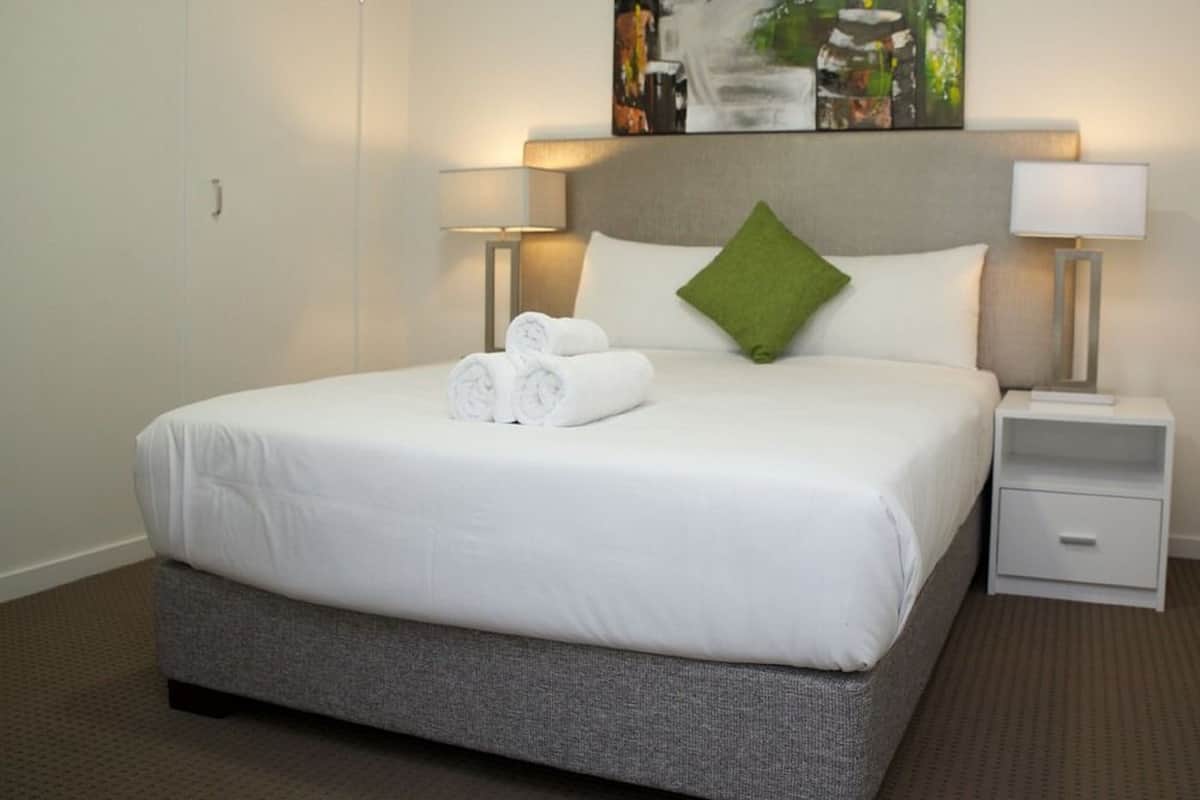 Ein Hotelzimmer mit einem großen Bett, zwei Nachttischen, einem grünen Kopfkissen und einem Bild an der Wand.