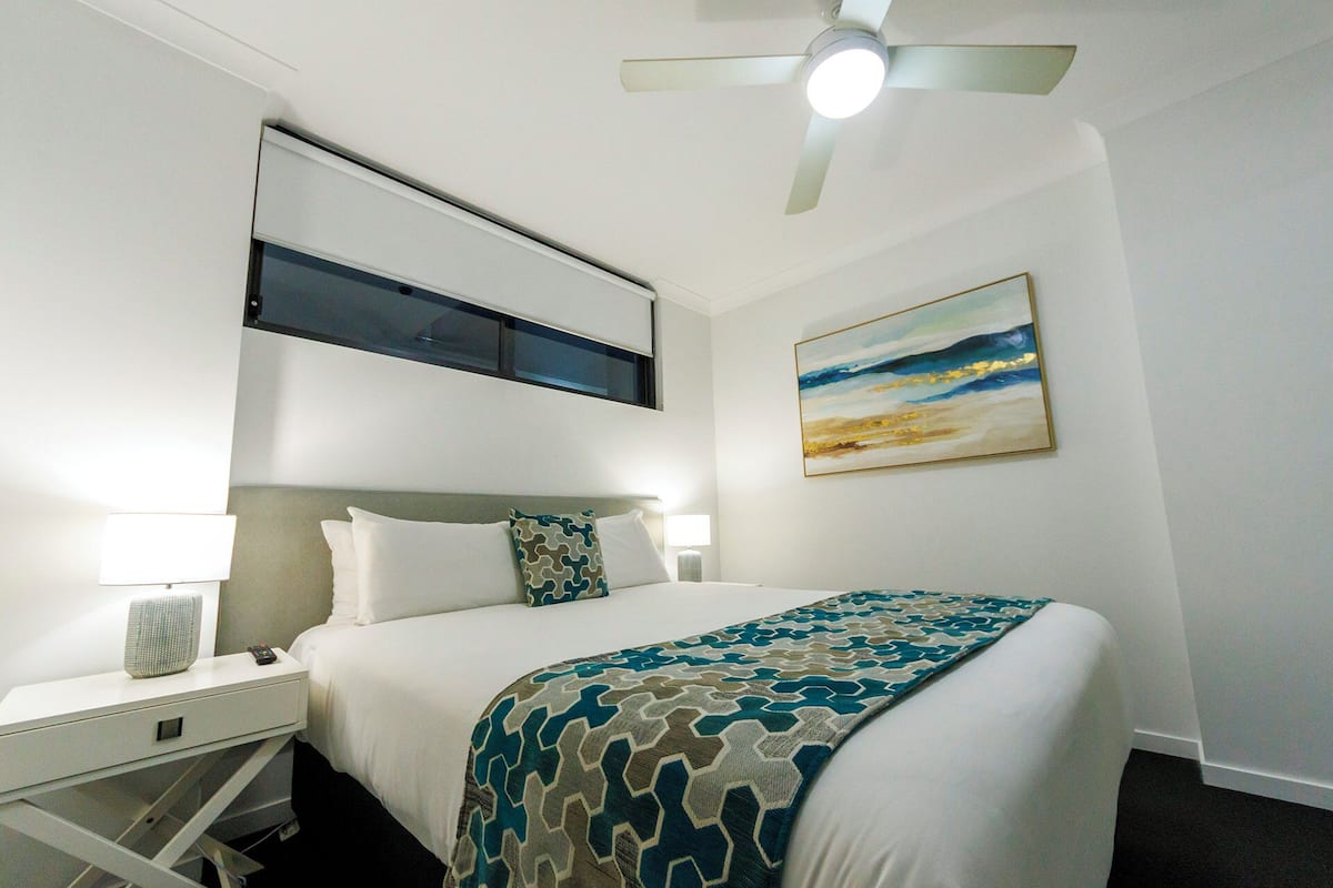 Ein Hotelzimmer mit Bett, Nachttisch, Lampe, Deckenventilator und einem Bild an der Wand.