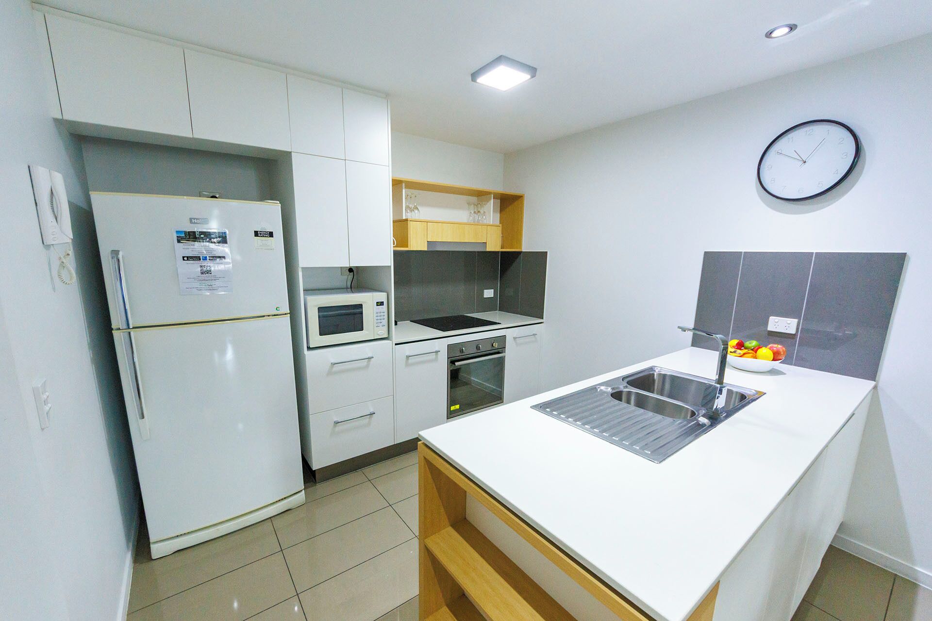 Une cuisine moderne avec des meubles blancs, un four à micro-ondes, un four traditionnel, un évier et une horloge au mur.
