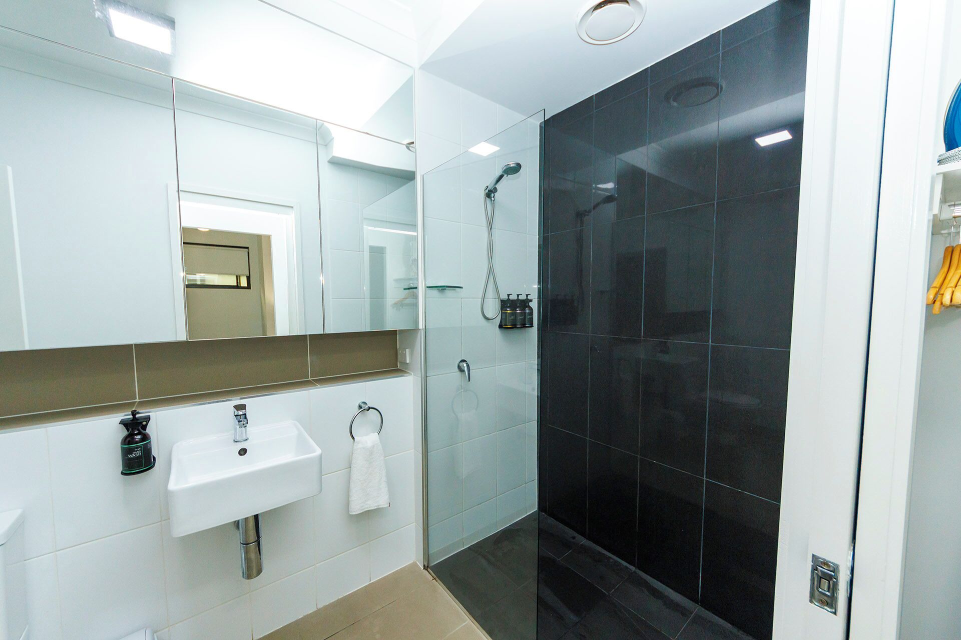Un baño moderno con un lavabo blanco, un espejo y baldosas de ducha negras.