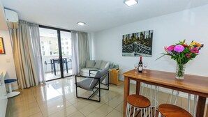 A modern living room with a sofa, a dining area with a table and chairs, a painting on the wall, and a vase with flowers. - Atrio Apartments (Fortitude Valley)