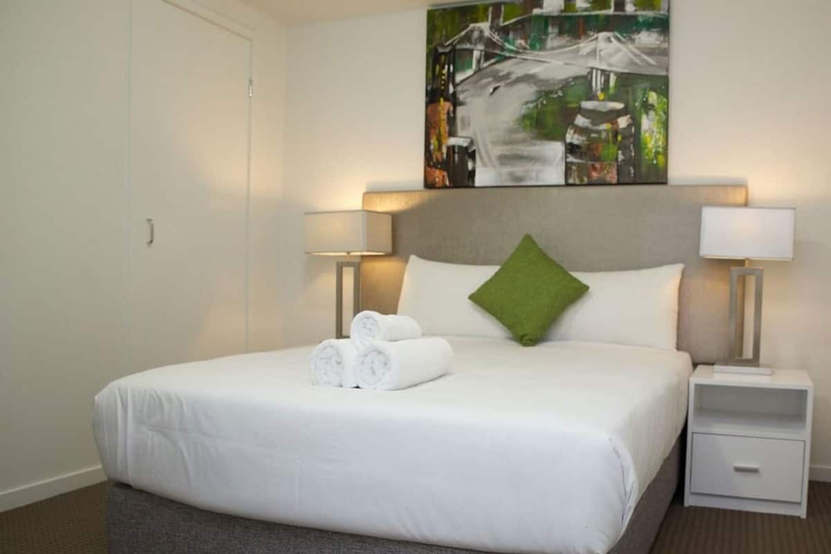 Ein Hotelzimmer mit einem großen Bett, zwei Nachttischen, einem grünen Kopfkissen und einem Bild an der Wand.