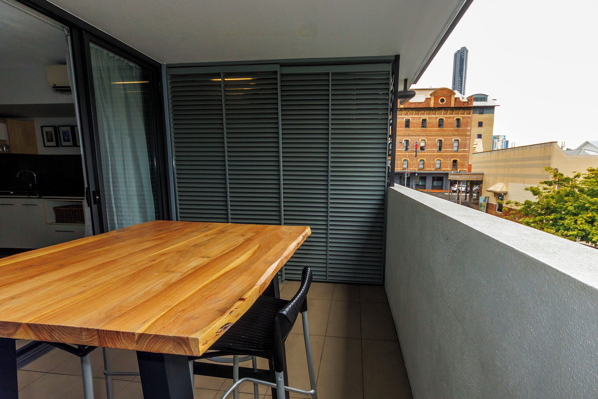 Un balcon avec une table et des chaises en bois, une porte coulissante et une vue sur un bâtiment doté d’un clocher.