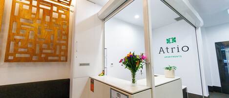 Ein Empfangsschalter mit Glastrennwand, einer Wandpaneele aus Holz und einem Schild für Atrio Apartments.
