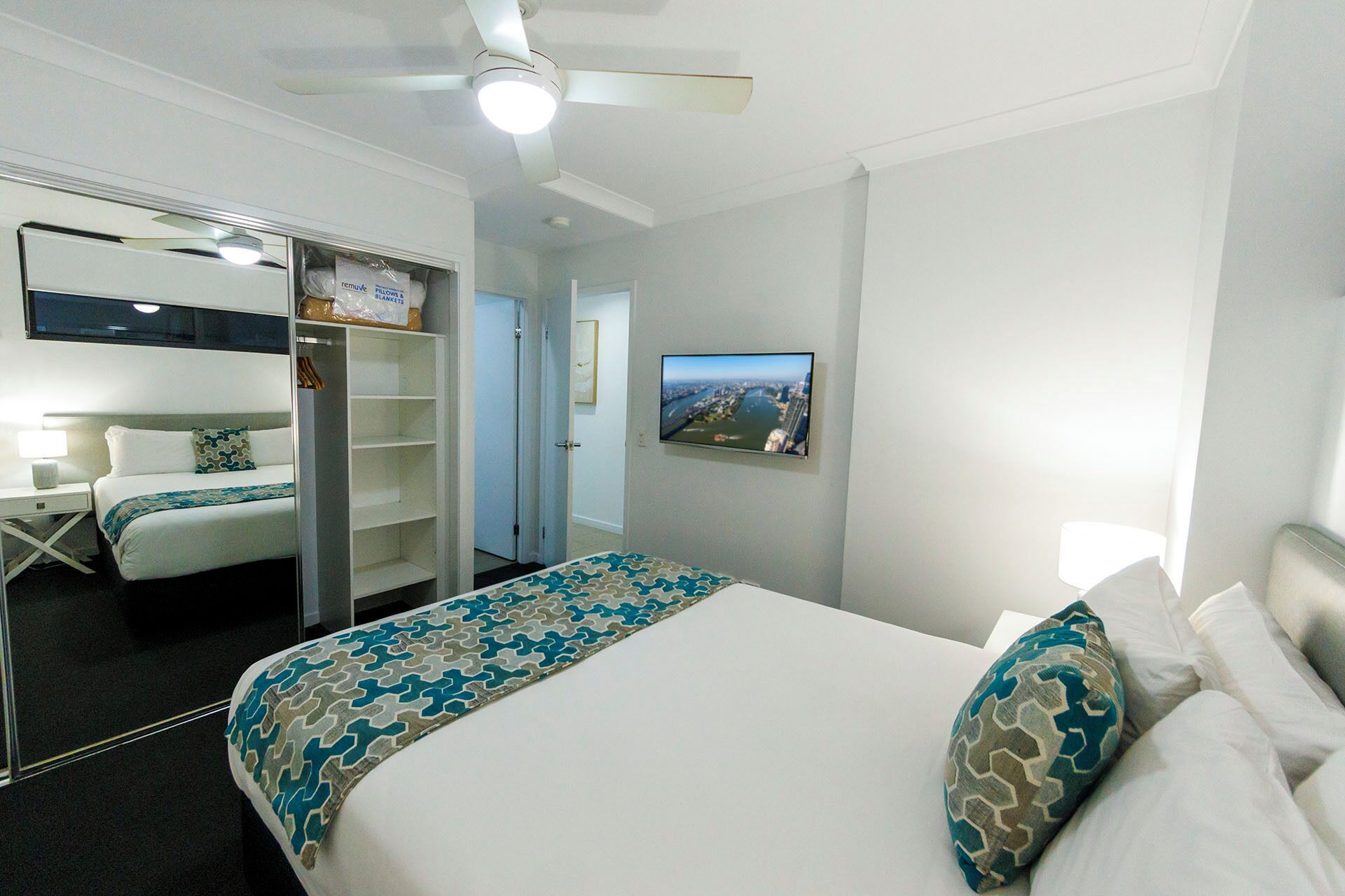 A hotel room with a bed, a wardrobe, a television, and a ceiling fan.