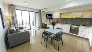 A modern kitchen with white cabinets, a dining area with a glass table, and a living area with a sofa and a TV. - Atrio Apartments (Fortitude Valley)