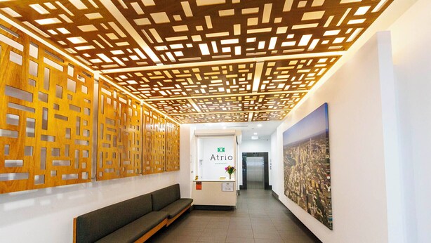 A hallway with a wooden decorative ceiling, a reception desk, a bench, and a cityscape painting. - Atrio Apartments (Fortitude Valley)