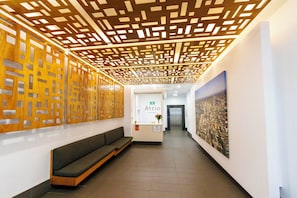 A hallway with a wooden decorative ceiling, a reception desk, a bench, and a cityscape painting. - Atrio Apartments (Fortitude Valley)