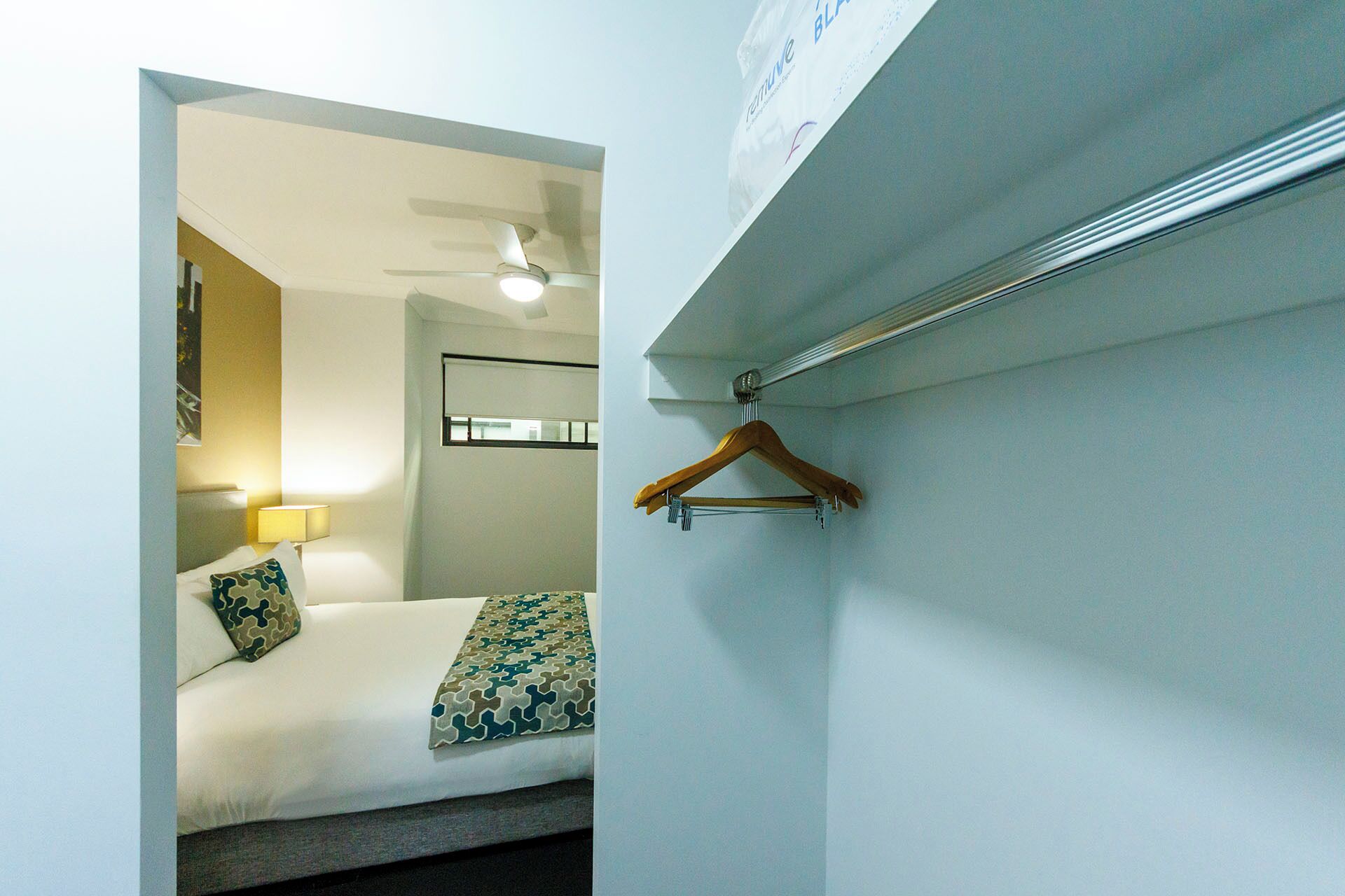 A hotel room with a bed, a hanging wooden hanger, and a ceiling fan.