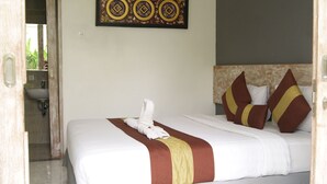 A hotel room with a neatly made bed, a headboard with decorative pillows, a wall-mounted artwork, and a bathroom visible through an open door. - Sugiras Living (Denpasar)