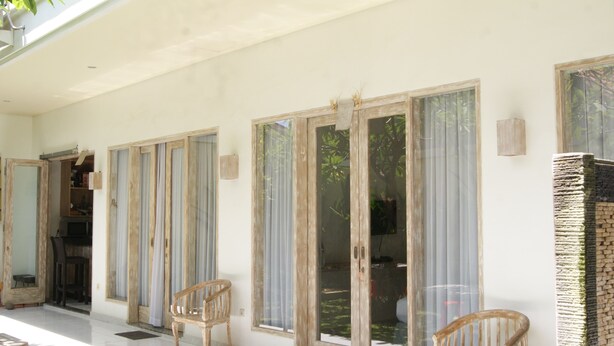Un porche cubierto con puertas corredizas de vidrio, sillas de madera y una pared de piedra.