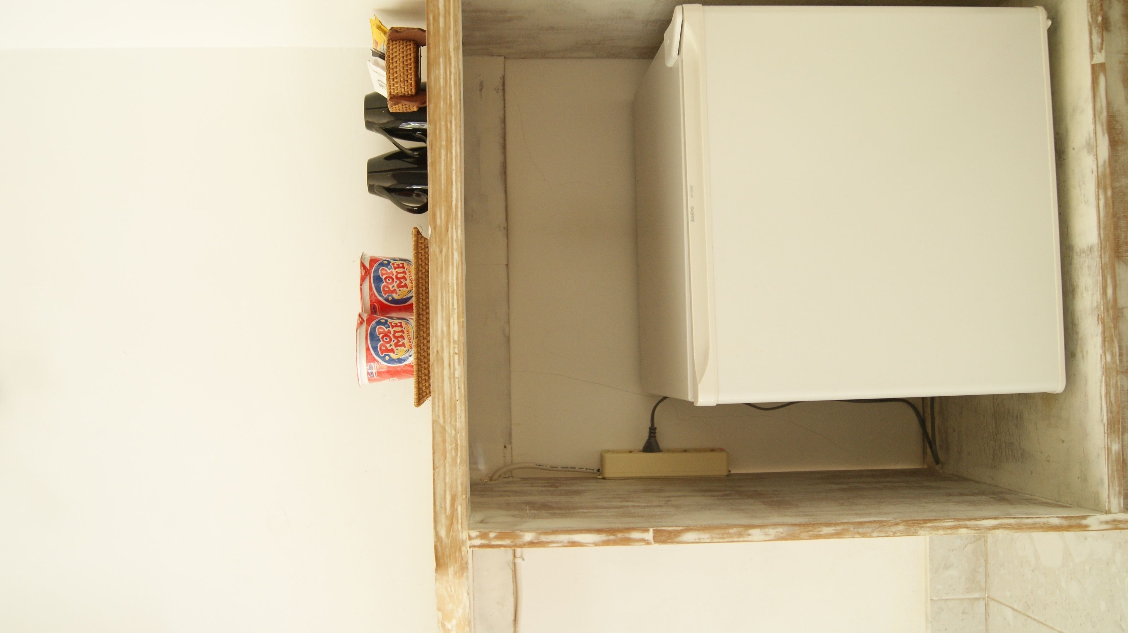 A kitchen with a white refrigerator, a wooden shelf with a waffle maker, and two cans of Pop Tarts.