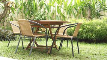 Una mesa de madera redonda con cuatro sillas de mimbre, rodeada de plantas verdes y césped exuberante.