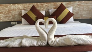 Habitación de hotel con cama, ropa de cama blanca, almohadas marrones y amarillas, y dos toallas dispuestas en forma de corazón.
