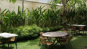 A patio area with a round wooden table and four chairs, surrounded by lush green plants and a tree. - Sugiras Living (Denpasar)