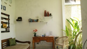 Una habitación con un escritorio de madera, una silla, una cama con almohada verde, un estante con libros y adornos, y una planta en maceta.