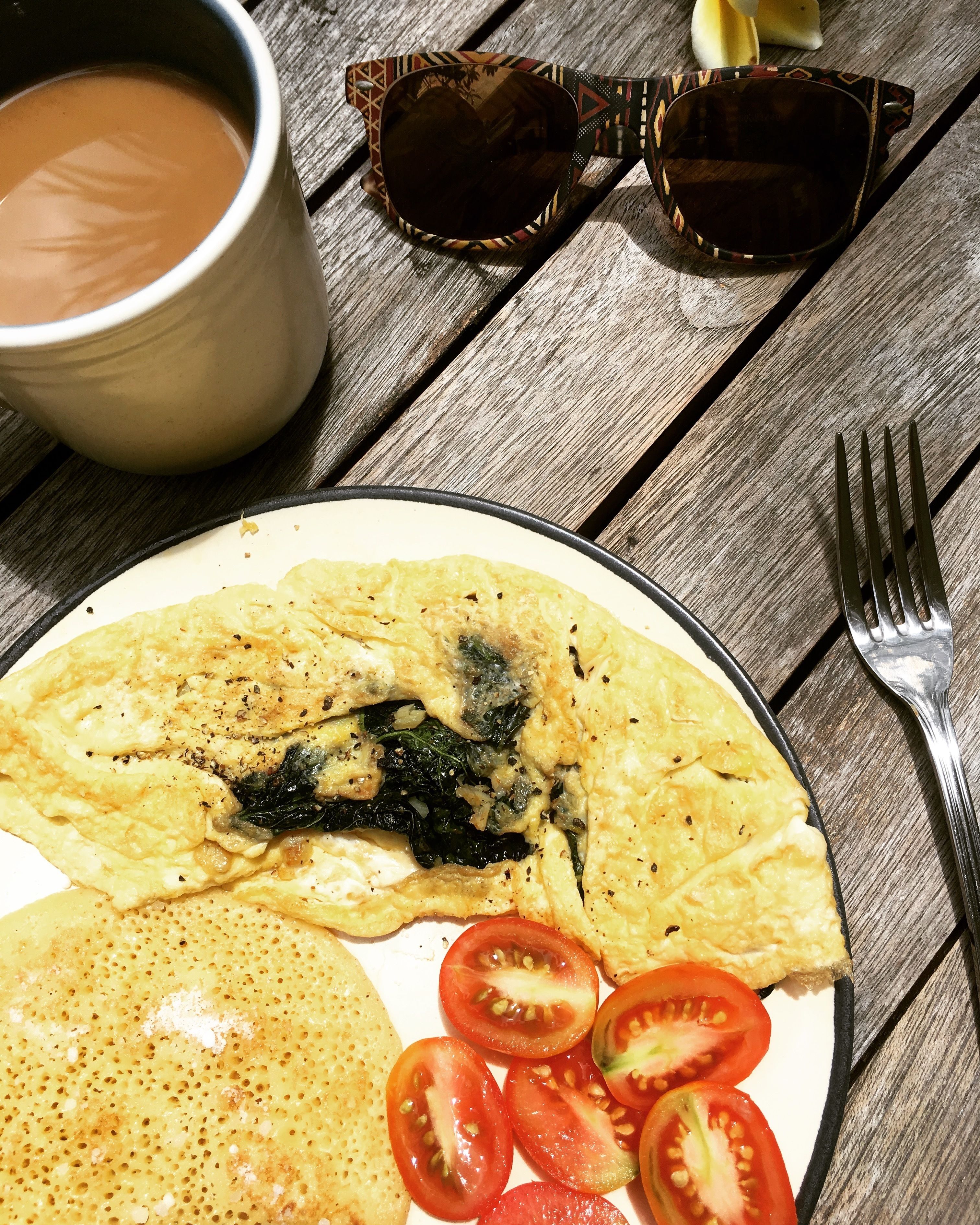A plate with an omelette, tomatoes, and a cup of tea on a wooden table.