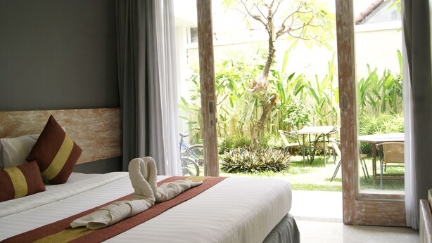 Habitación de hotel con cama, ventana y vistas a un jardín y zona de estar al aire libre.