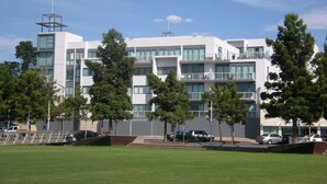 A modern multi-story building with a flat roof, large windows, and a parking area in front. - The Waterfront Apartments, Geelong (Geelong)