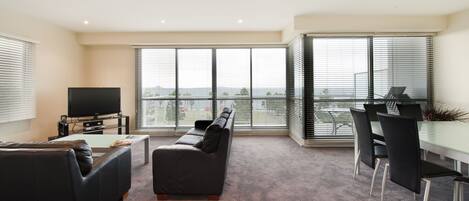 A modern living room with a sofa, a coffee table, a TV, and a dining area with chairs and a glass table.