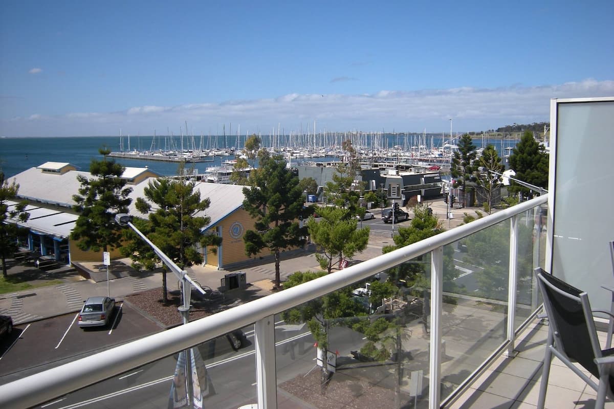 Un puerto deportivo con numerosas embarcaciones amarradas, cielo despejado y vista al mar.