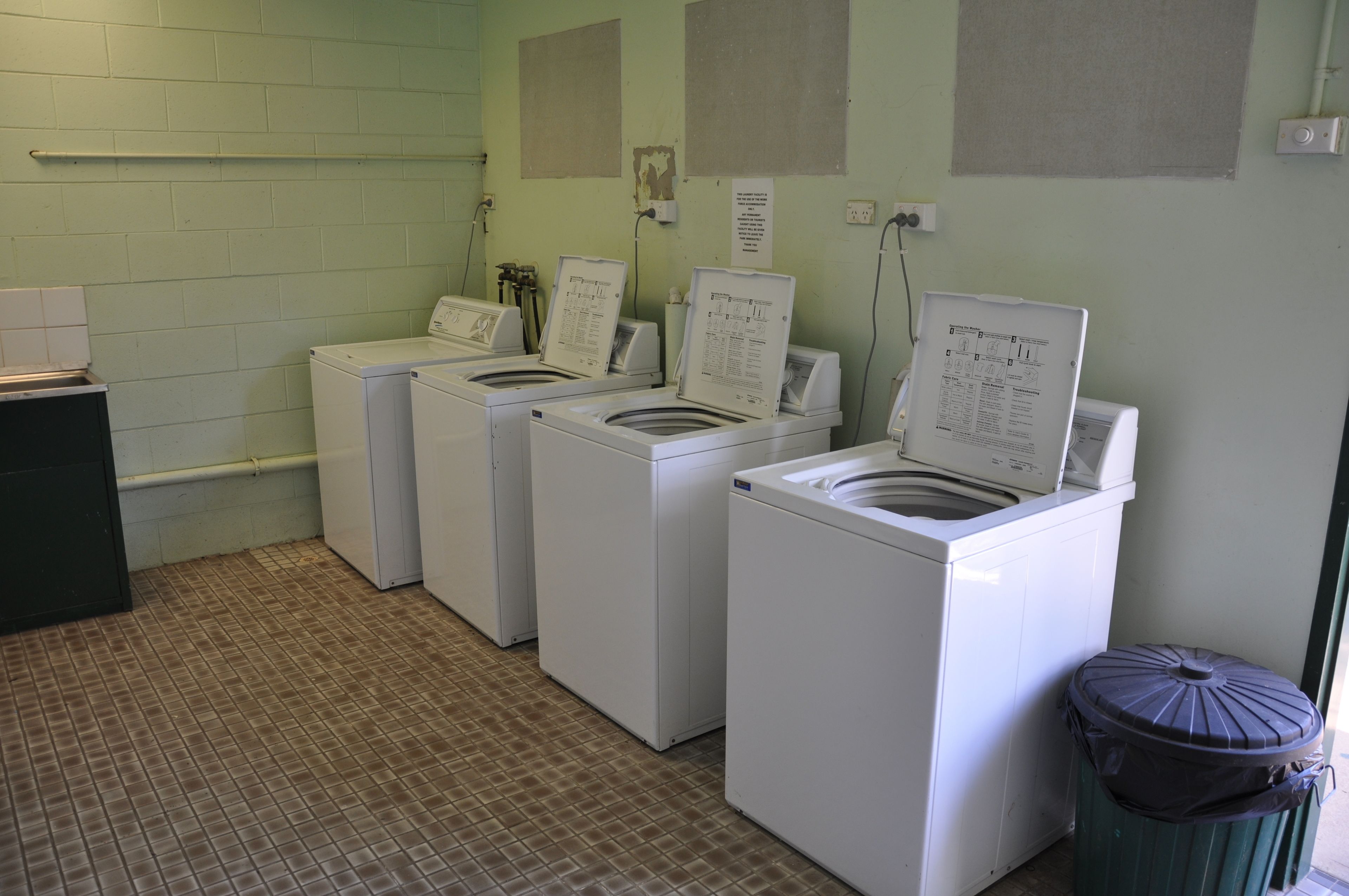 A laundry room with four white washing machines and a trash bin.