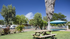 A picnic table with a blue umbrella, surrounded by grass and trees. - Discovery Parks - Mount Isa (Winston)
