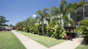 A residential area with a sidewalk, parked cars, and lush greenery including palm trees and shrubs. - Discovery Parks - Mount Isa (Winston)