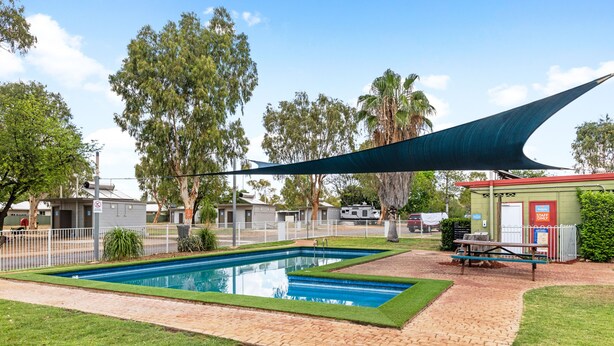 A swimming pool with a surrounding brick walkway, a shaded area with a table and chairs, and a small building with a 'Staff Only' sign. - Discovery Parks - Mount Isa (Winston)