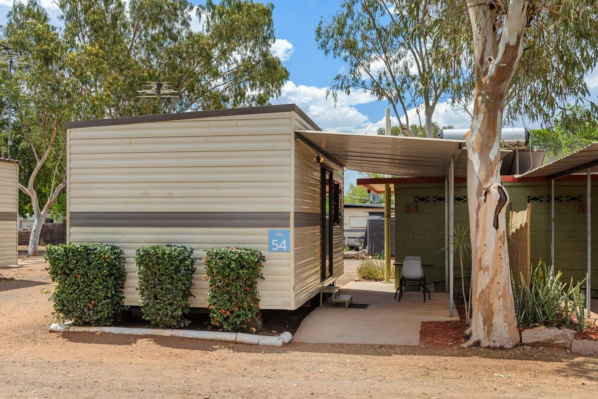 A mobile home with a covered patio, number 54, surrounded by greenery and trees.