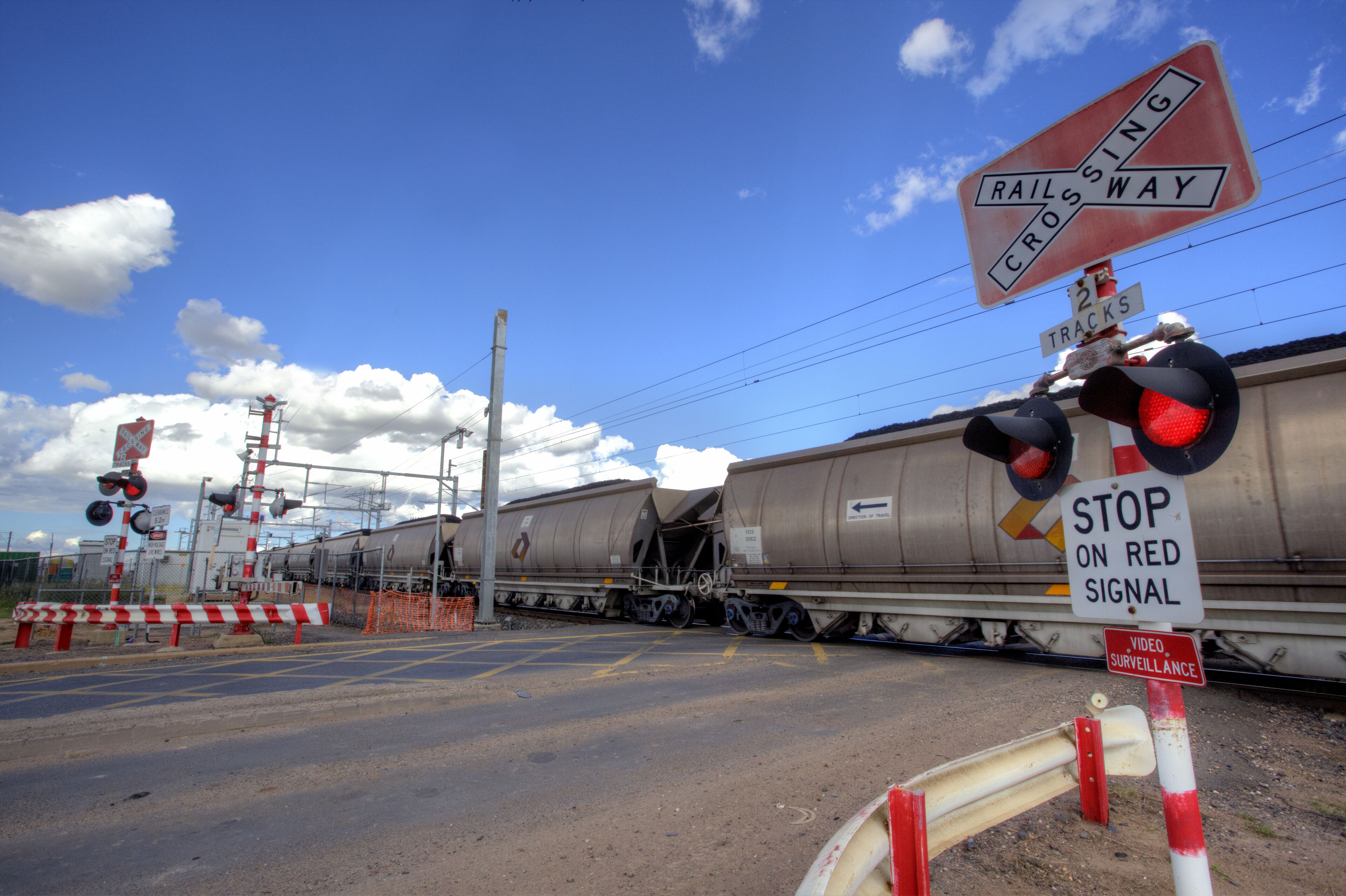 Un paso de tren con un cartel que dice 'STOP ON RED SIGNAL', un cartel de 'RAILROAD CROSSING' y un cartel de 'VIDEO SURVEILLANCE'.