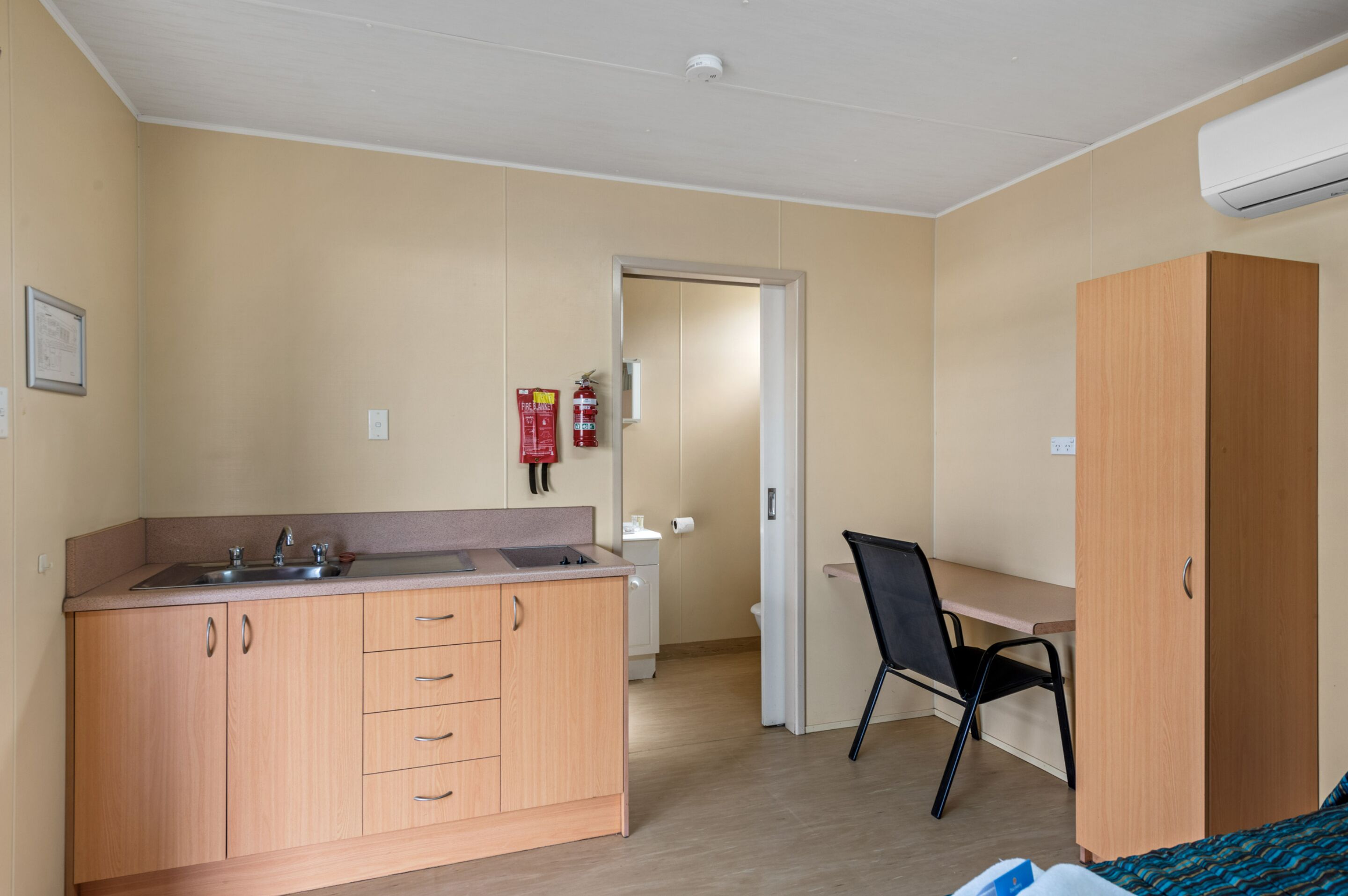 A compact room with a kitchenette, a single bed, a desk, and a chair.