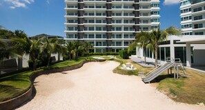 A beachfront hotel with multiple balconies, a sandy beach, palm trees, and a children's play area. - The Sea Condominium (Sam Roi Yot)