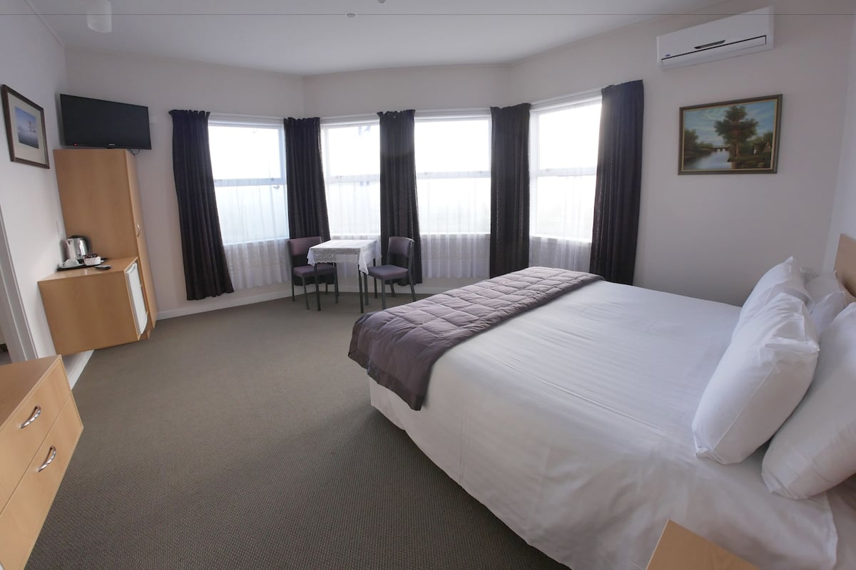 Una habitación de hotel con cama, escritorio, silla, televisor y ventana con cortinas.