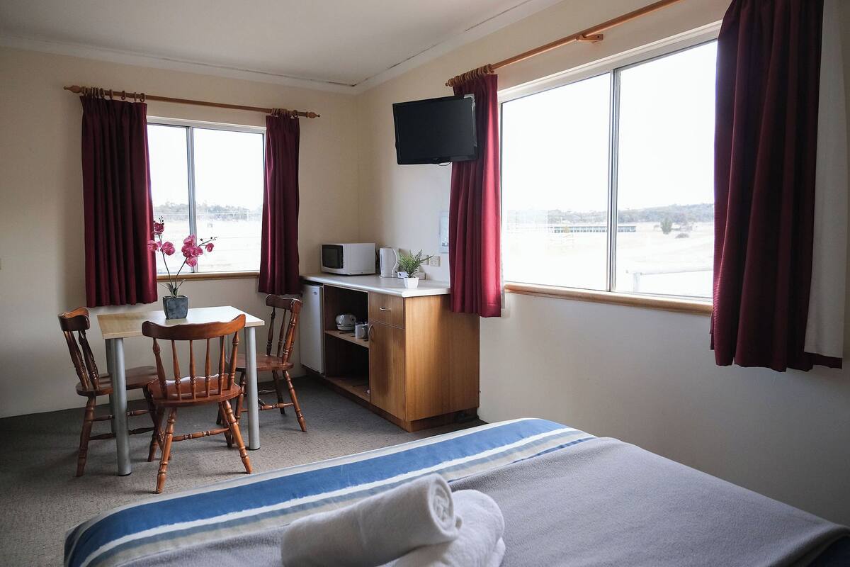 Een hotelkamer met een bed, een bureau met een computer en een televisie, een stoel, en uitzicht op een waterpartij.