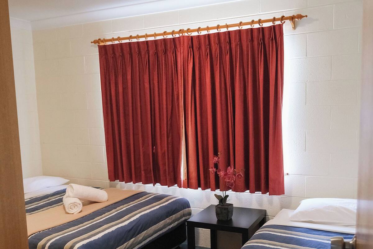 Een hotelkamer met twee bedden, een kleine tafel en een raam met rode gordijnen.