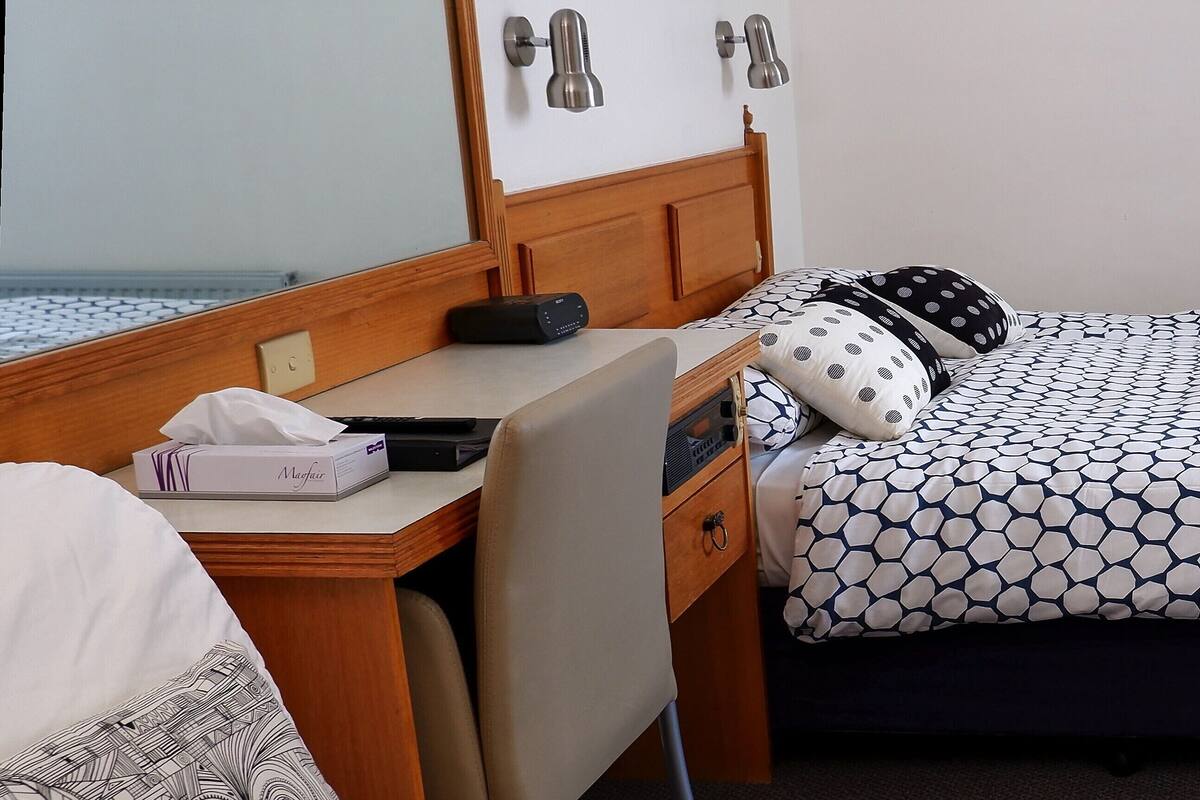 A hotel room with a bed, a desk, a chair, a bedside table, and a nightstand.