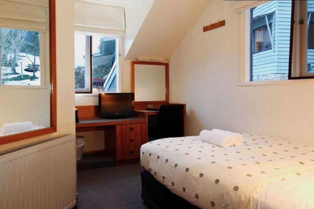 A bedroom with a bed, a desk, a chair, a laptop, and a window.