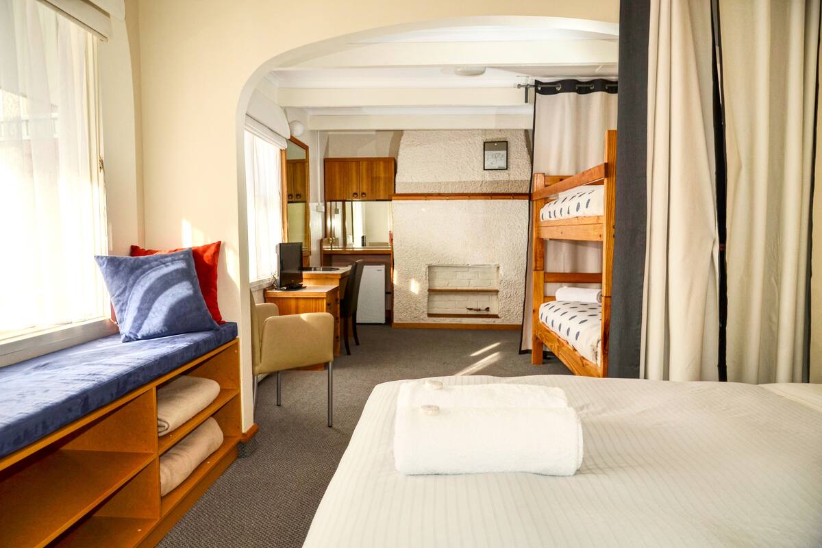 A cozy RV bedroom with a bed, a seating area with a bench, a desk, and a fireplace.