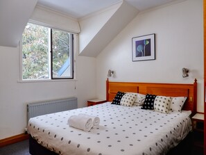 A bedroom with a bed, a window, a radiator, and a framed picture on the wall. - Alpenhorn (Thredbo)