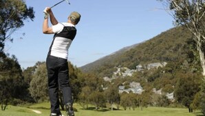 A person playing golf on a course with a hilly background and houses. - Alpenhorn (Thredbo)