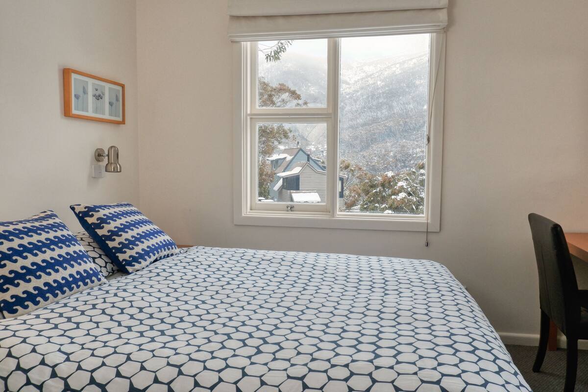 A bedroom with a large bed, a window with a view of a snowy landscape, and a framed picture on the wall.