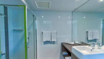 Un baño moderno con cabina de ducha de vidrio, un espejo grande y un mueble de tocador con lavabo.