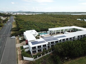 A modern hotel with a swimming pool, solar panels, and a view of a road and water body. - Mackay Oceanside Central Hotel (East Mackay)